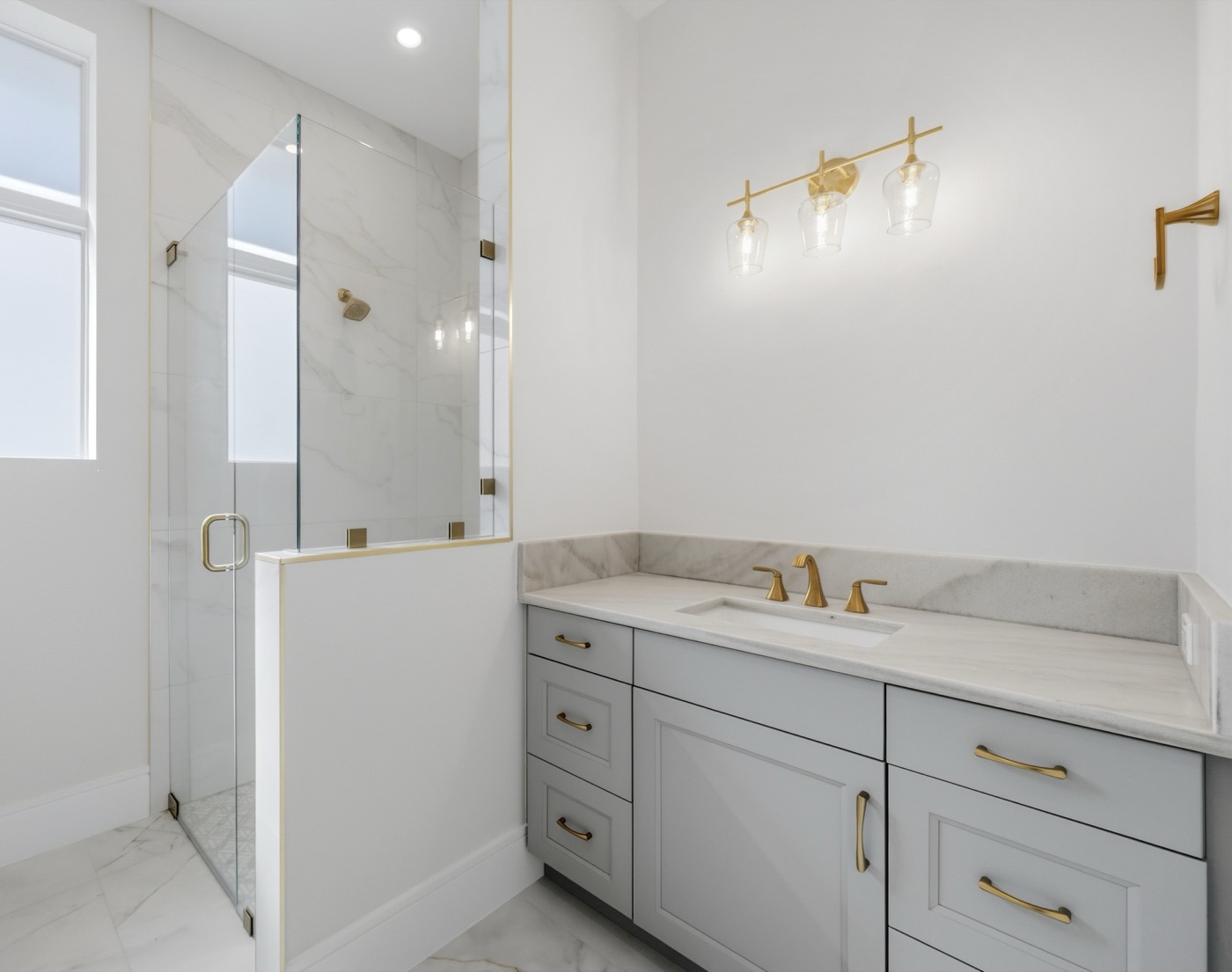 Bright bath with book-matched Calacatta marble corner shower trimmed in brass — Modern Residence