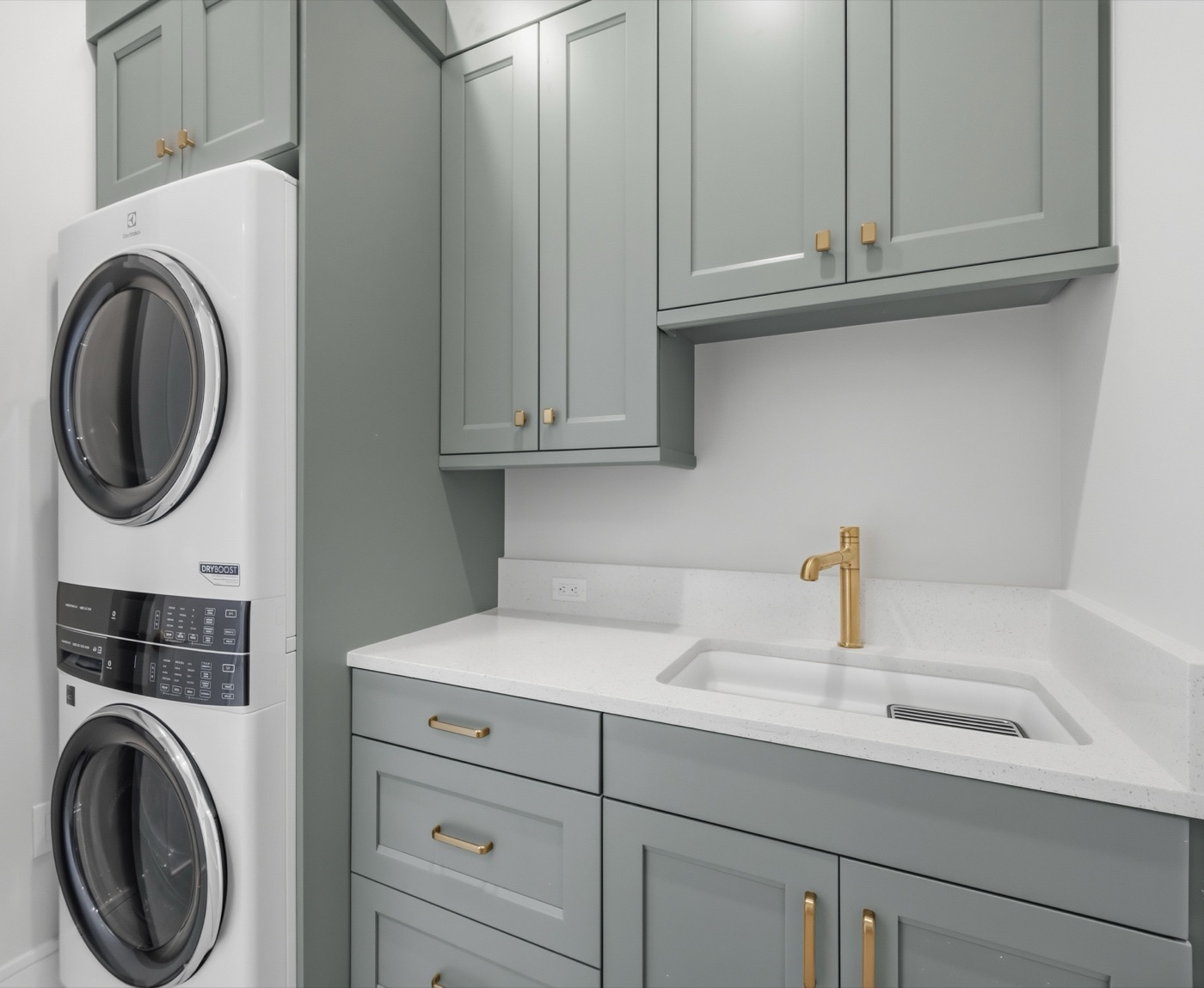 Refined laundry suite in sage-green shaker cabinetry with brushed-brass pulls — Modern Residence