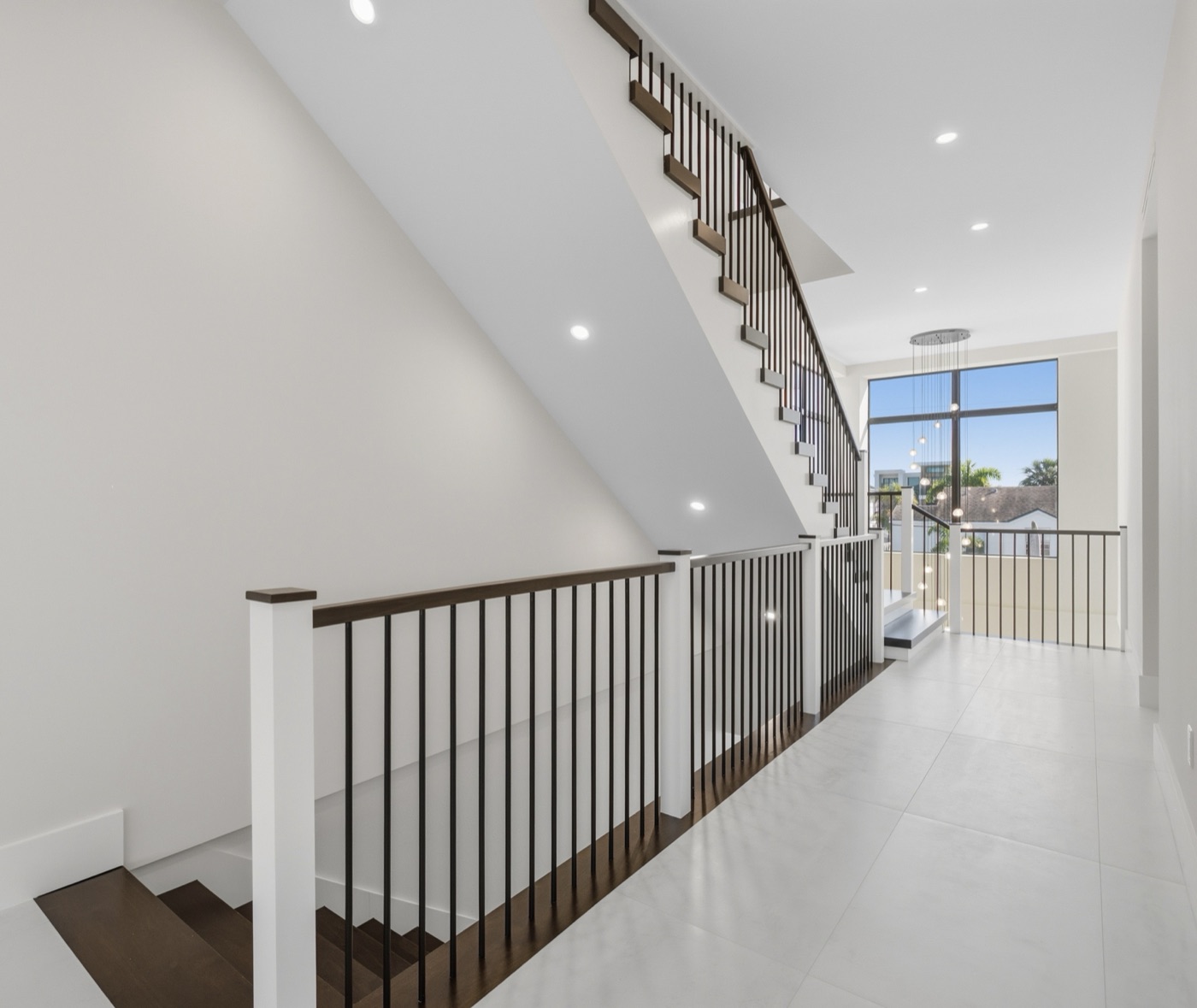 Upper landing of walnut staircase with slim black railing and crystal pendant chandelier — Modern Residence