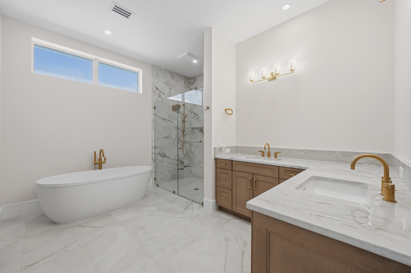 Spa-like primary bath with freestanding soaking tub and brushed-gold filler — Coastal Residence